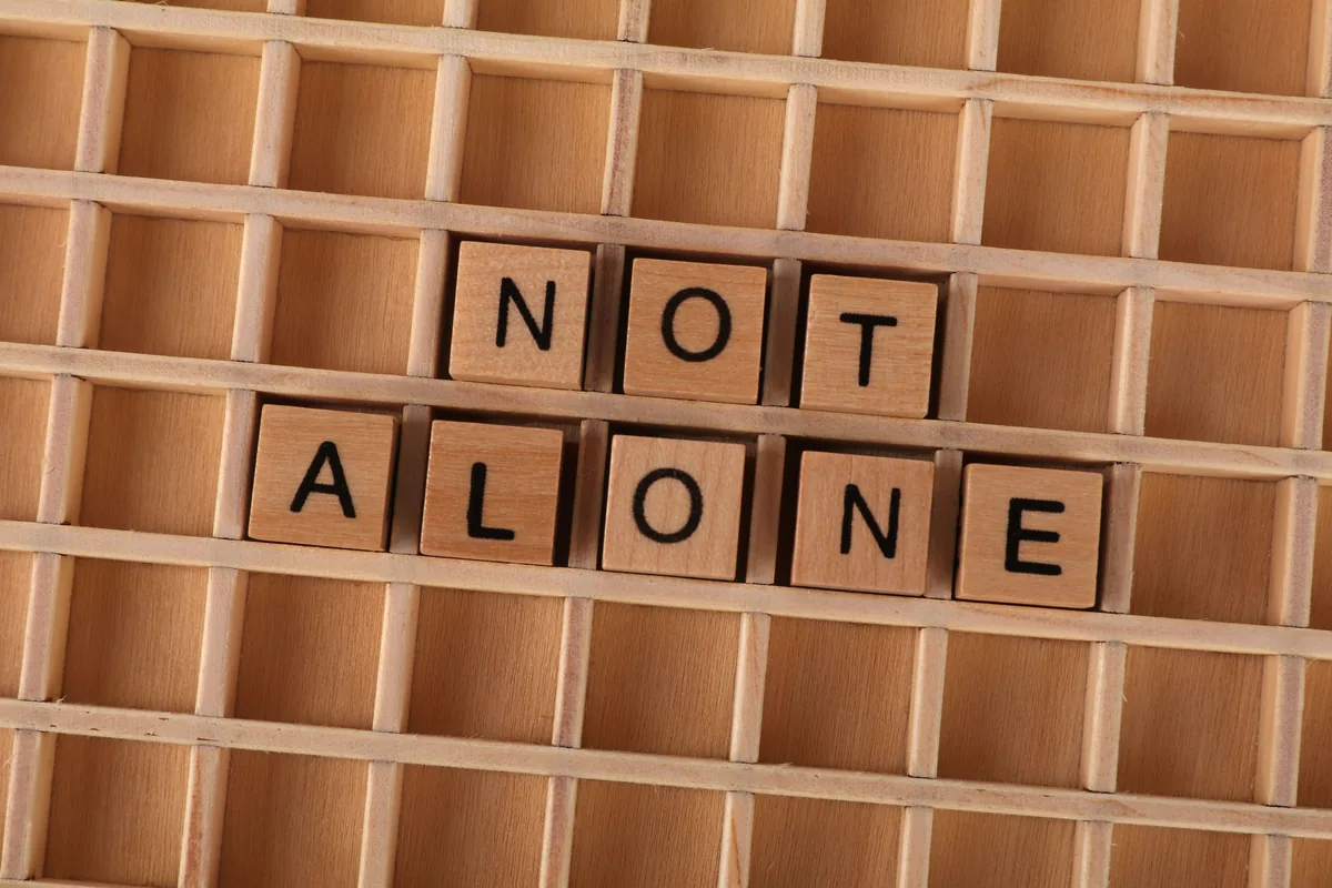 Wooden Scrabble tiles spelling Not Alone on a wooden grid background, conveying support and connection.