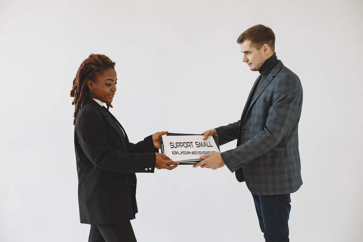Two business professionals exchanging a box labeled Support Small Businesses in a studio setting.
